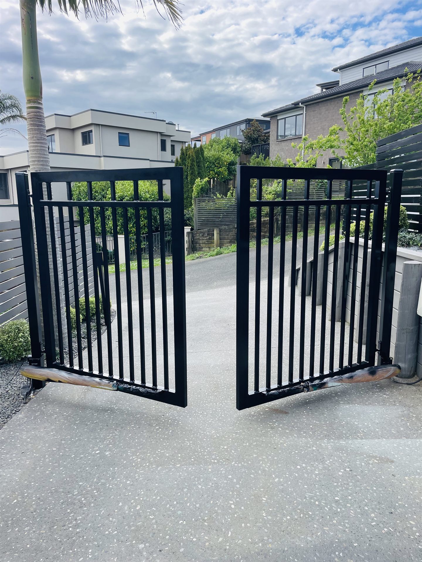 Freshly painted black double swing gates at an Auckland driveway entrance