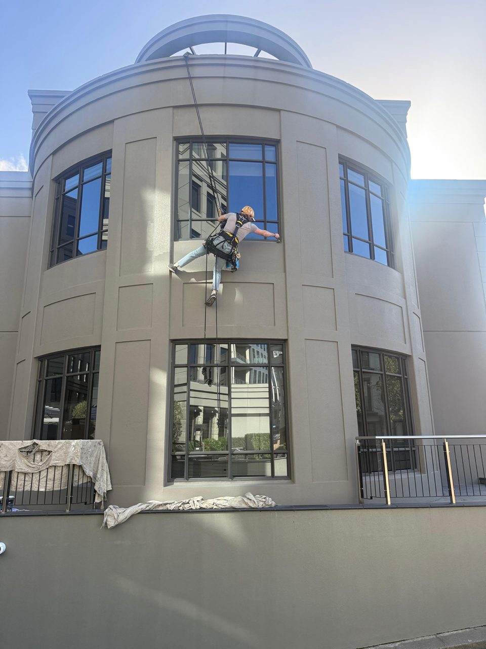 Rope-access painter abseiling down the curved tower to coat the facade above the entrance