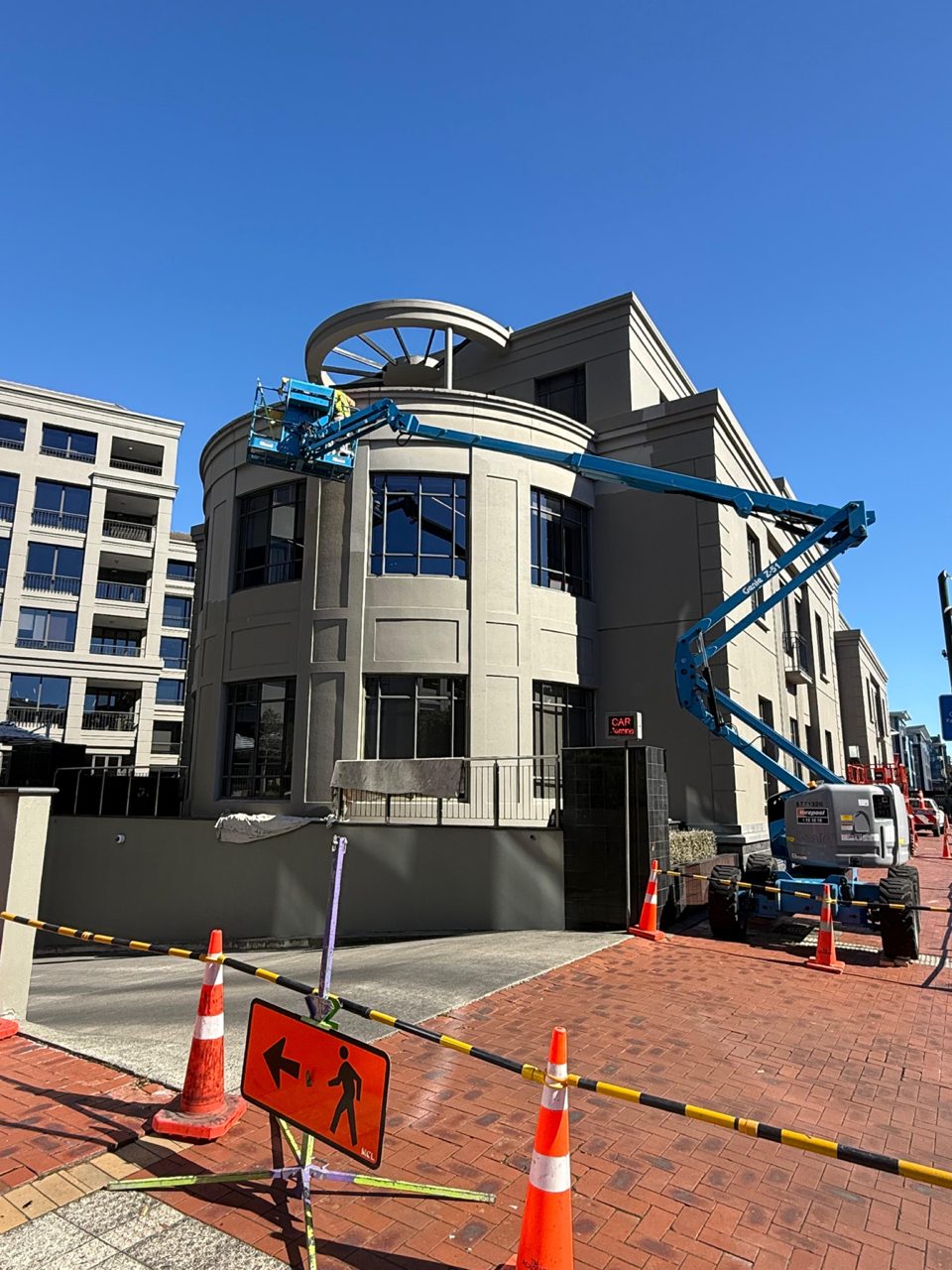 Boom lift reaching the curved corner tower of the CBD building during the repaint