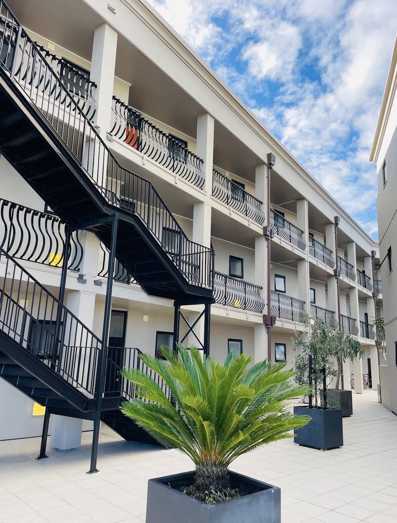 Repainted apartment complex courtyard with black steel stairs, balcony runs and planted palms