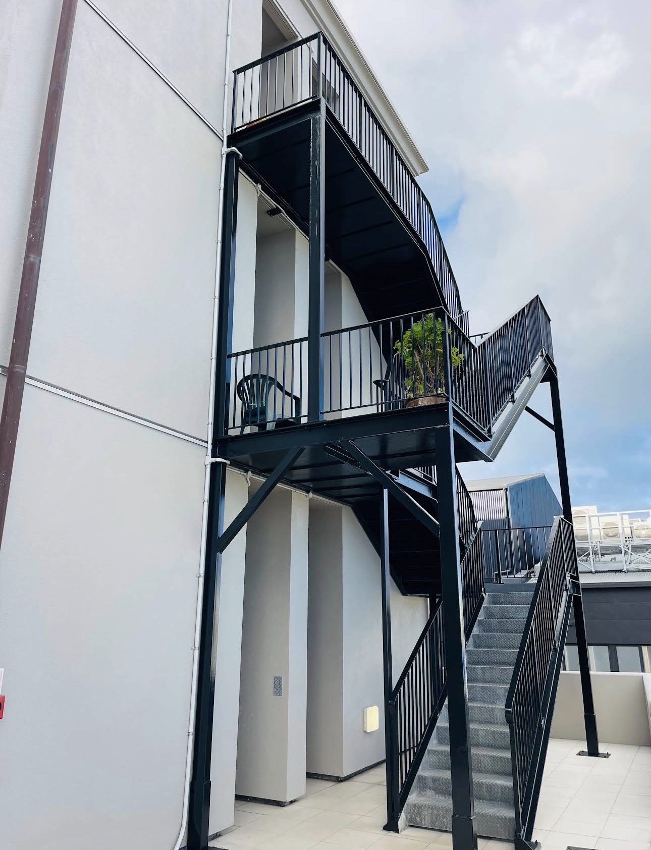 Repainted black steel fire stair against the pale plastered apartment wall